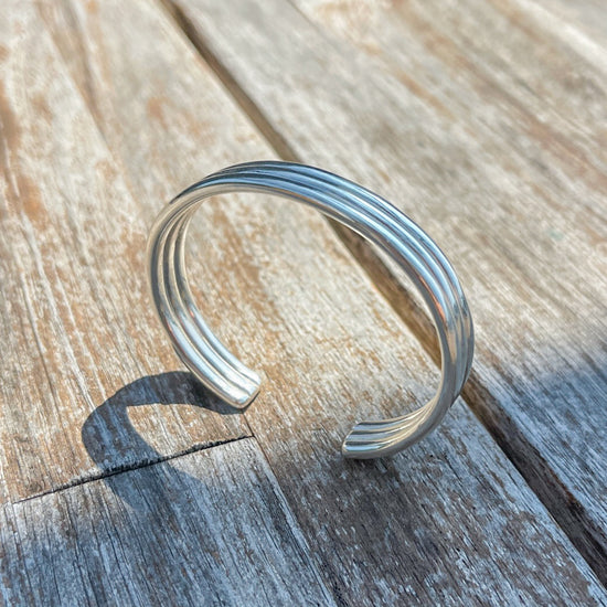 The Bauble Cuff in sterling silver on a wooden background in the sunshine